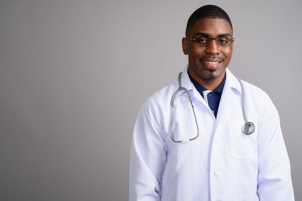 Young handsome African man doctor against gray background